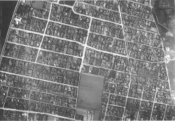 Fugleperspektivet tydeliggør parcelhuslivet som et liv mellem vejene. Kvarterets trafikale infrastruktur indrammer typisk 18-24 parceller i rektangulære mønstre. Det er et rationelt rum tænkt i forlængelse af en linial - eller er det billedet af en printerplade til en pc.
Luftfoto fra Risbjerggårds Villaby 1935.
(Foto HLA)